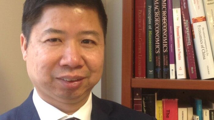 Tony Fang, professeur d'économie à l'université Memorial, est à côté d'une bibliothèque.