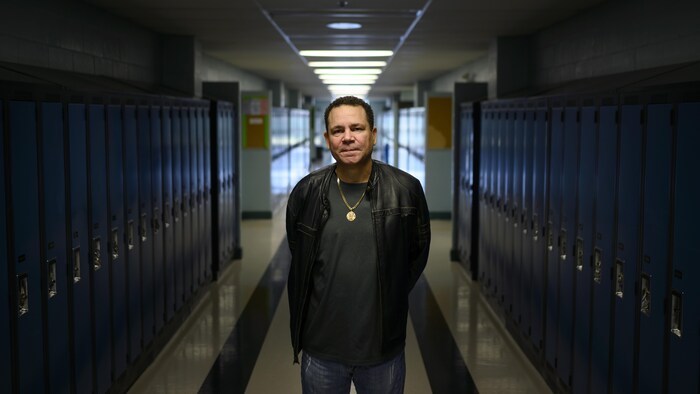 Un homme adulte debout dans le corridor d'une école entre deux rangées de casiers.