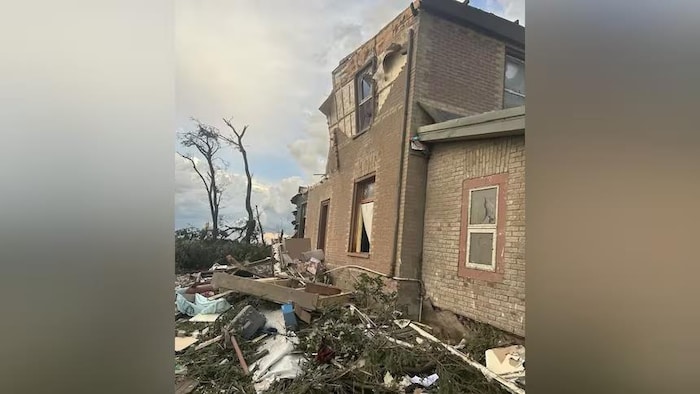 Une maison en briques centenaire a été fortement endommagée par une tornade. De nombreux débris jonchent le sol.