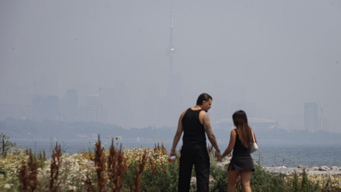 Un homme et une femme devant un panorama de Toronto obscurcie par la fumée.