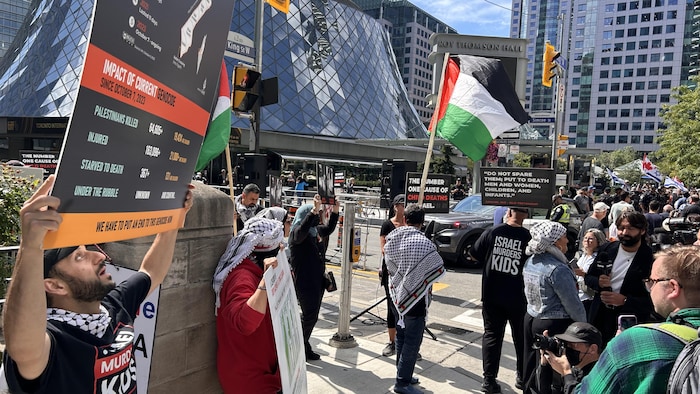 Des manifestations propalestiniennes avec des drapeaux et des pancartes devant la salle Roy Thomson Hall.