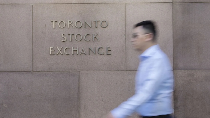 Un homme en chemise marche devant la bourse de Toronto.