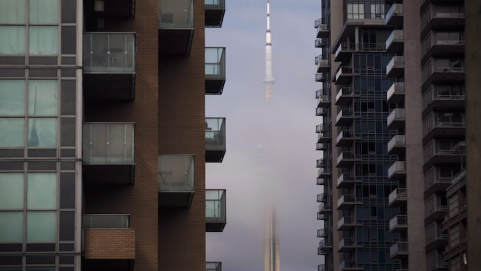 La tour du CN, dans le brouillard, entre deux immeubles à condos.