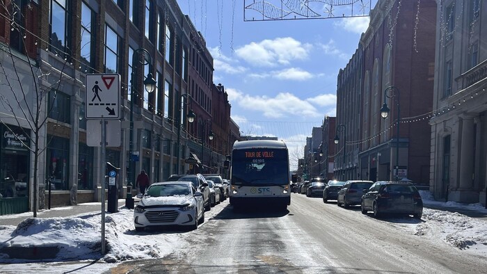 Un autobus de la Société de transport de Sherbrooke avance sur la rue Wellington, à Sherbrooke. Sur son enseigne lumineuse est indiqué « Tour de ville ».