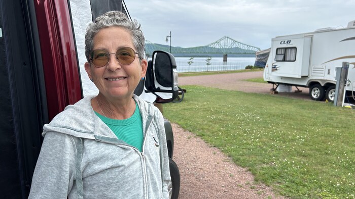 Une femme sourit à la caméra, dans un terrain de camping.