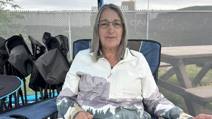 Une femme assise sur une chaise de camping, sourit à la caméra.