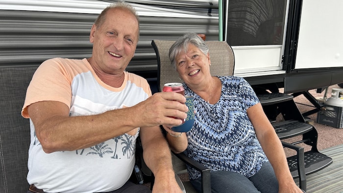 Deux personnes âgées sourient à la caméra, tenant un verre dans leurs mains en signe de «santé».