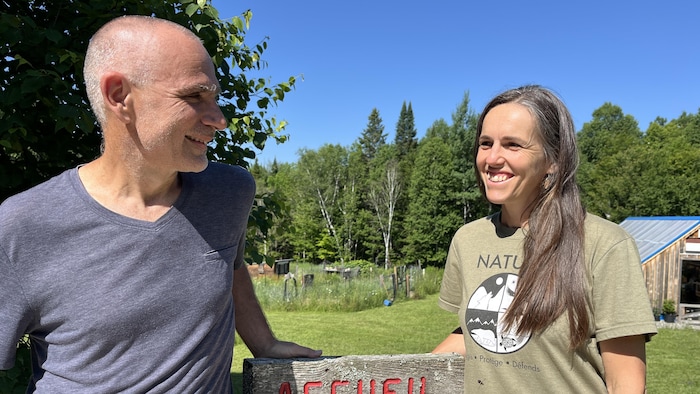 Les deux se regardent dans les yeux en souriant, devant la pancarte qui indique la réception de leur lieu d'hébergement.