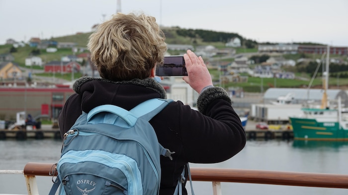 Une touriste prend une photo du port de Cap-aux-Meules à bord du traversier.