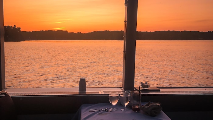 Une table avec deux verres devant la fenêtre d'un bateau de croisière sur le lac Ontario près de Kingston, au coucher du soleil.