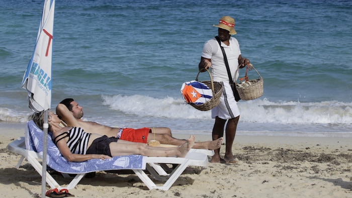 Des touristes prennent un bain de soleil tandis qu'un vendeur propose des cerfs-volants décorés du drapeau cubain.