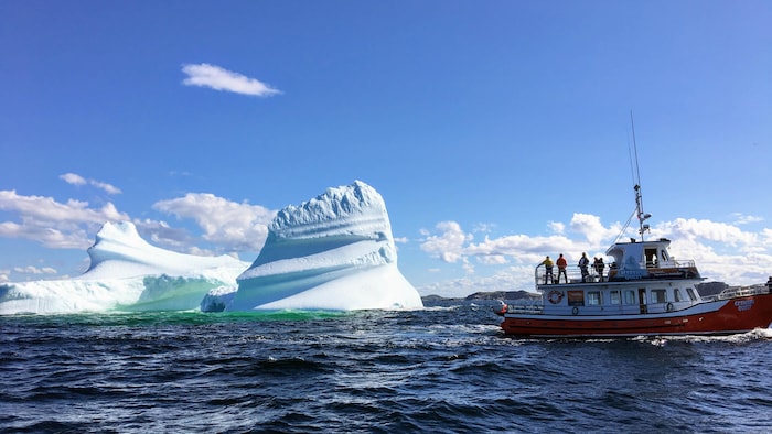 Un petit bateau avec quatre personnes debout sur le pont s'approche d'un iceberg.