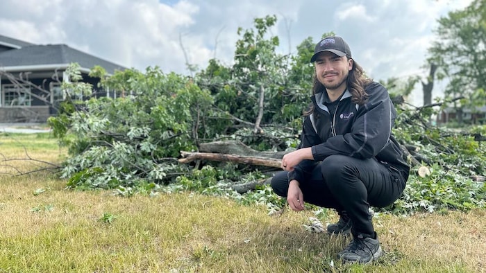 Aaron Jaffe accroupi devant plusieurs arbres et branches abattus à la suite d'une tempête à Talbotville, en Ontario.