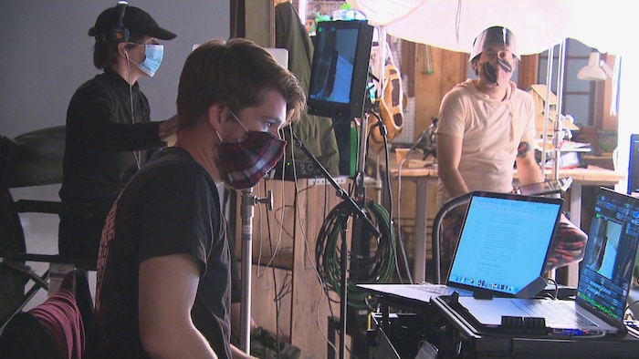 Trois personnes travaillent sur un plateau de tournage en portant un masque.