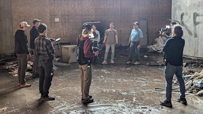 Une équipe de tournage filme trois personnes dans un lieu qui semble délabré.