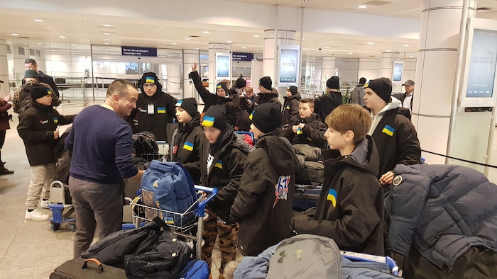 Sean Bérubé est entouré des jeunes et de leurs valises. Ils sont dans le hall de l'aéroport de Montréal.
