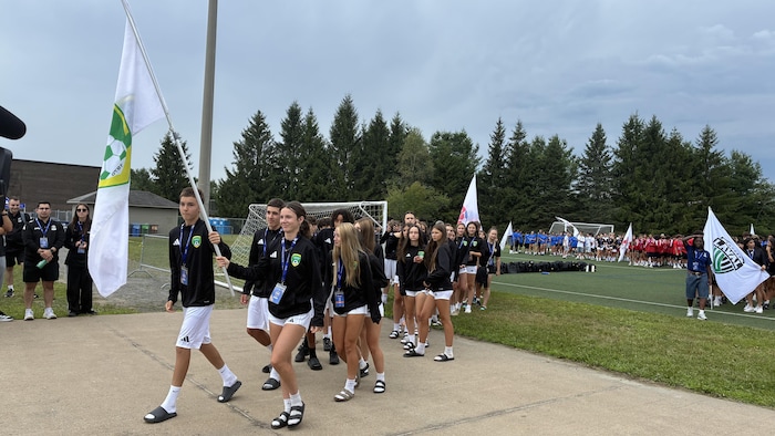 Une délégation de joueurs et joueuses font leur entrées dans le stade avec un drapeau. 