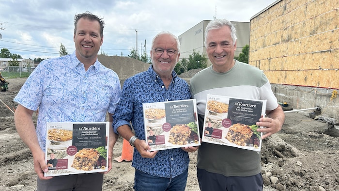 Michel Barrette qui pose avec le directeur général et le fondateur de l'entreprise avec des tourtières dans les mains. 