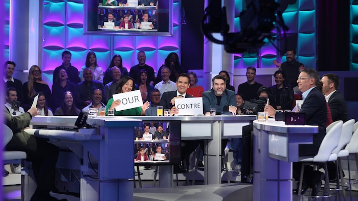 Ruba Ghazal et Charles Milliard montrent des cartons « POUR » et « CONTRE » aux côtés de Mc Gilles sur un plateau télé.