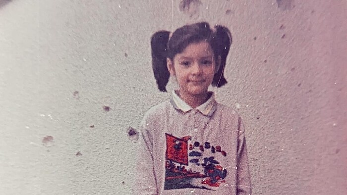 Ana Mocnaj pendant la guerre sur son balcon à Sarajevo, devant un mur criblé de trous d'obus et autres projectiles.  