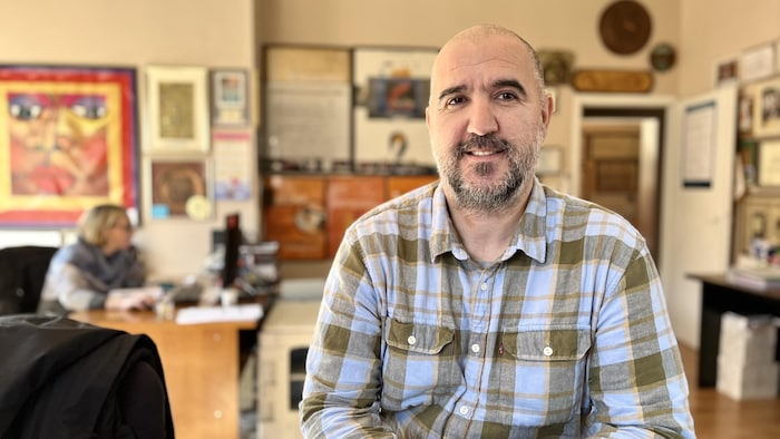 Un homme en chemise à carreaux assis dans un bureau.
