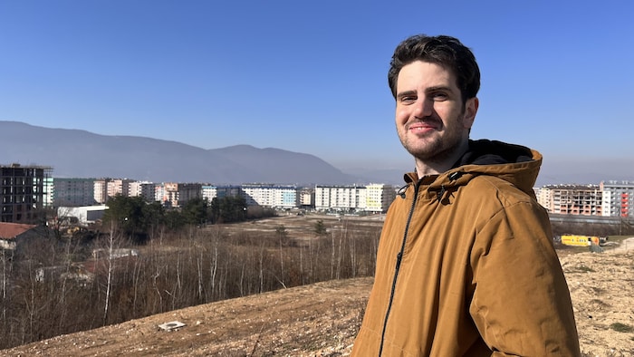 Jeune homme devant un paysage d'immeubles et de montagnes.