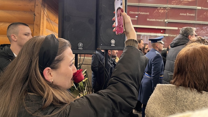 Une jeune femme avec une rose rouge et un cellulaire tenu devant elle.