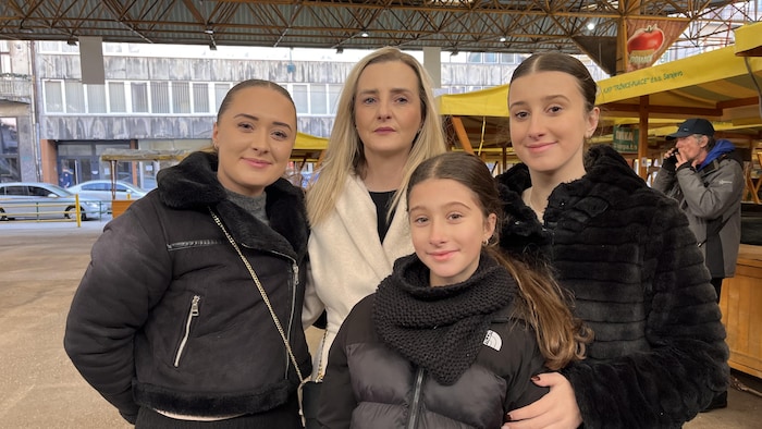 Une femme aux cheveux blonds et en manteau blanc entourée de trois jeunes filles.