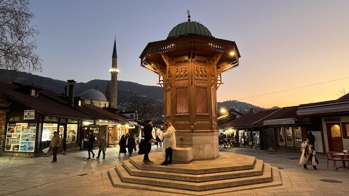 Minaret et fontaine sur une place publique, au coucher du soleil.