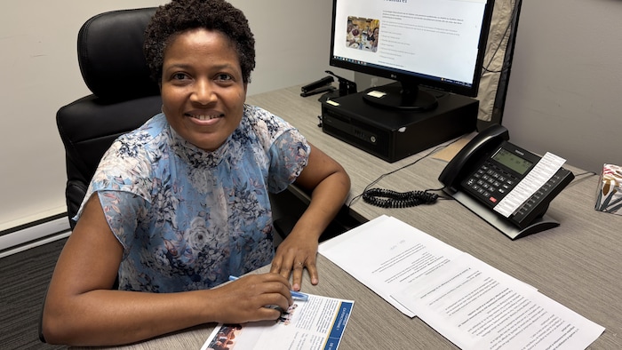 Une dame sourit alors qu'elle est assise à son bureau devant des dépliants du programme.