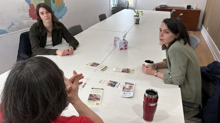 Trois personnes discutent autour d'une table dans une salle conférence.