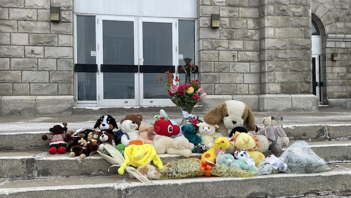 Des peluches et des fleurs sur le parvis de l'église.