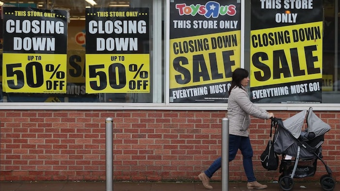 A woman pushing a pram in front of a store announcing up to 50% markdowns due to its closing.