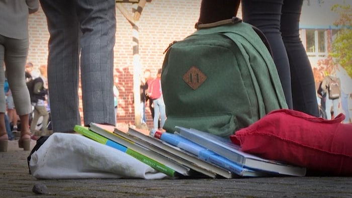 Un sac d'école et des livres déposés au sol dans une cour d'école. 