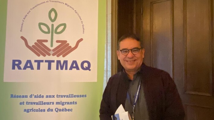 Melvin Méndez se tient debout à côté d'une grande affiche de l'organisme RATTMAQ.