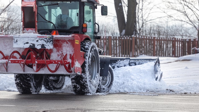 Un tracteur pousse de la neige dans une rue.