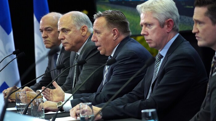 Les cinq hommes assis à une table derrière des micros pendant une conférence de presse.