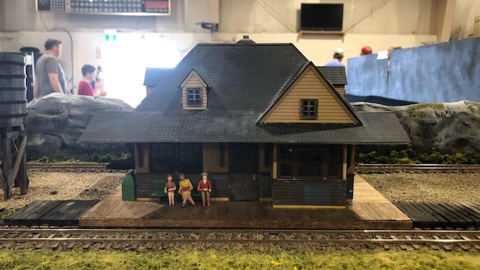 Un décor miniature représente une maison devant laquelle trois femmes sont assise sur le quai devant des rails de chemins de fer.