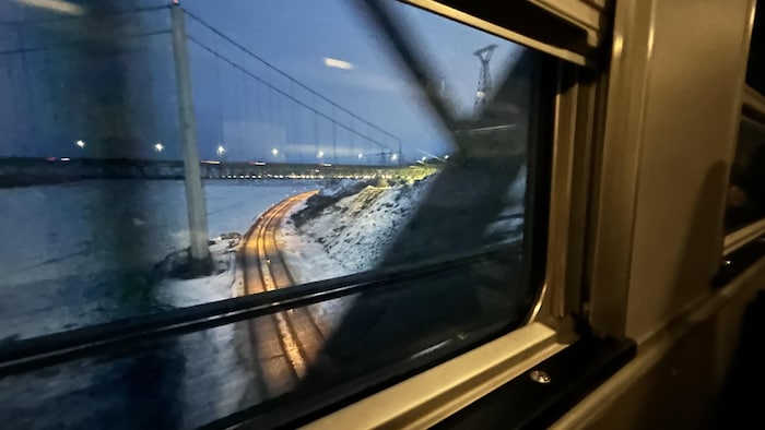 Vue de l'intérieur d'un train qui traverse un pont au petit matin.
