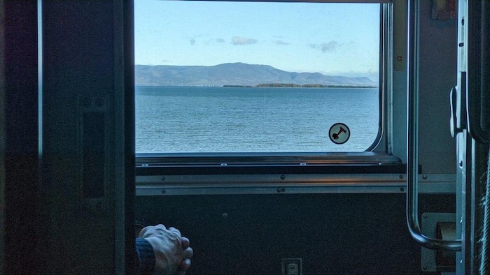 L'intérieur de la cabine d'un train. Un lac et une montagne sont visibles de la fenêtre. 
