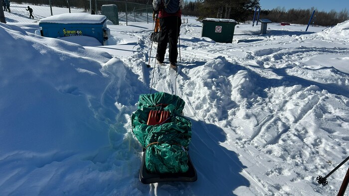 Une personne en ski de fond tire un traîneau avec du matériel, dont une pelle.