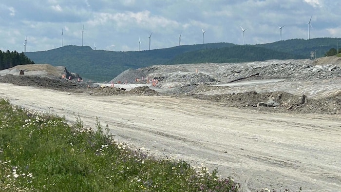 Un chantier de construction pour une autoroute. En arrière-plan, on voit des éoliennes sur des collines.