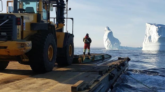 Une barge transportant un camion navigue près d'un glacier.