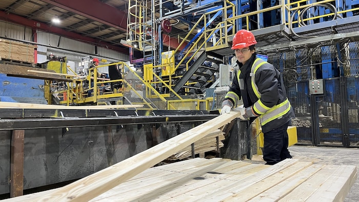 Un travailleur soulève une planche de bois dans une usine de bois-œuvre. 