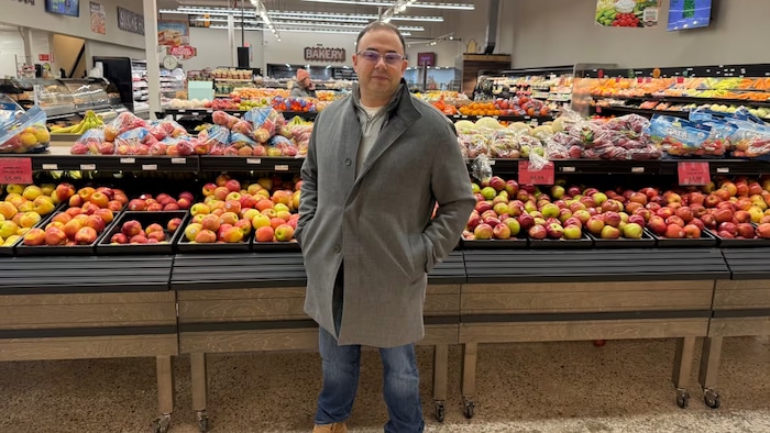 Un homme debout devant des fruits dans une épicerie.