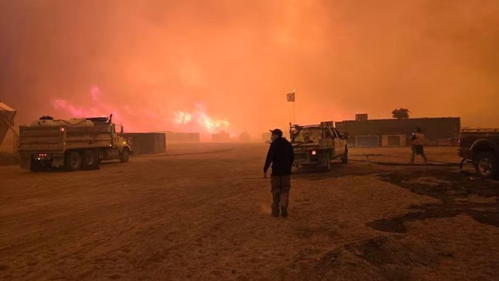 Un homme debout pendant qu'on voit un feu de forêt qui brûle au loin.