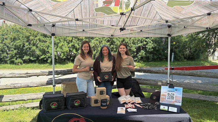 Les trois femmes posent à leur kiosque avec leurs objets promotionnels.