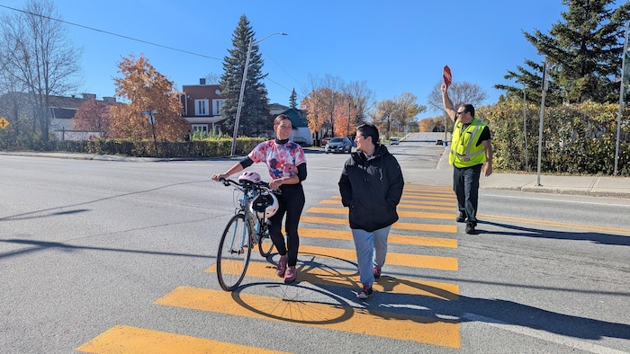 Un brigadier fait passer une personne à vélo et une autre à pied.