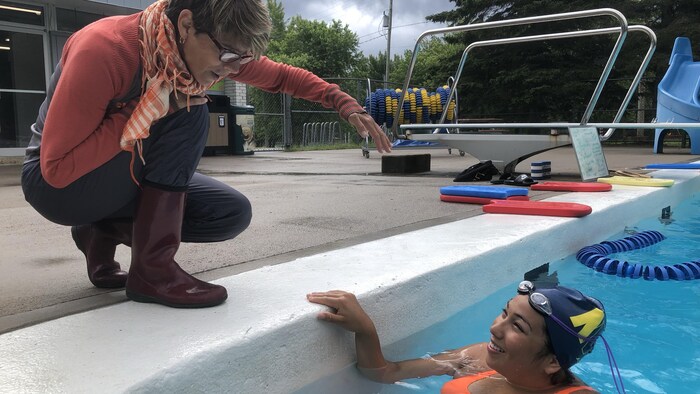 Alexann Petiquay, dans une piscine, s'adresse à son entraîneuse accroupie sur le bord.