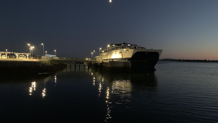 Un traversier près du quai, la nuit. Les lumières des lampadaires se reflètent sur l'eau.